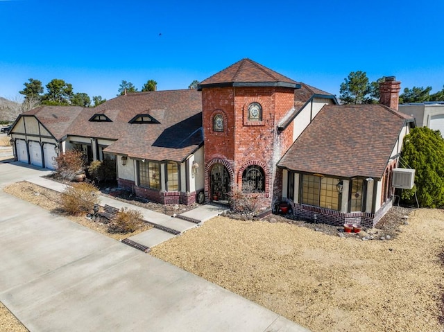 tudor house featuring a garage, roof with shingles, concrete driveway, and brick siding