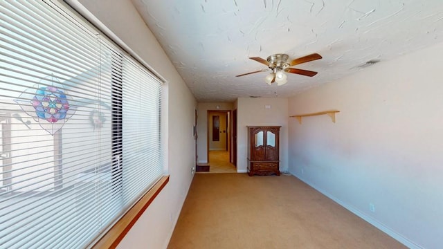 unfurnished room with light carpet, visible vents, baseboards, ceiling fan, and a textured ceiling