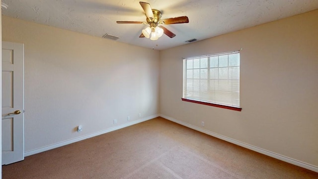 carpeted empty room with a ceiling fan, visible vents, and baseboards