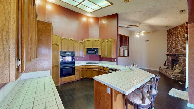 kitchen featuring dark wood-type flooring, a brick fireplace, a sink, a peninsula, and black appliances