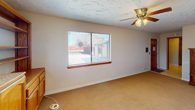 spare room with a ceiling fan, light carpet, a textured ceiling, and baseboards