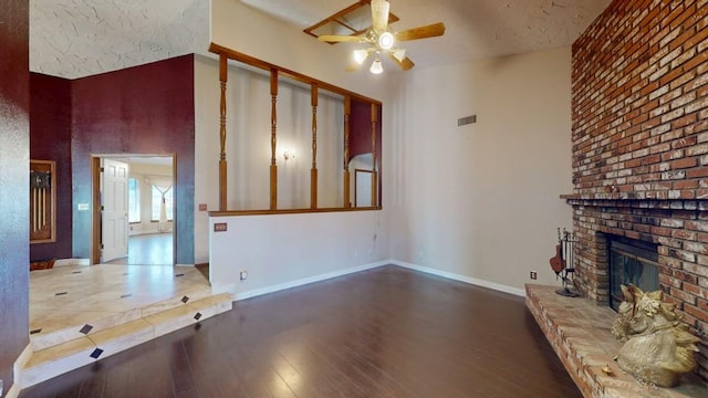 unfurnished living room featuring a high ceiling, wood finished floors, a ceiling fan, baseboards, and a brick fireplace