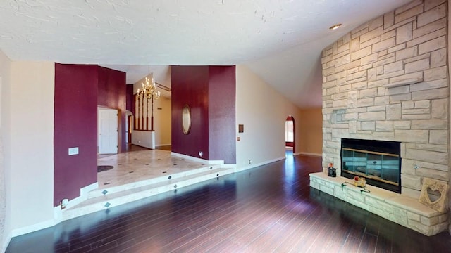 unfurnished living room featuring arched walkways, a fireplace, vaulted ceiling, wood finished floors, and baseboards