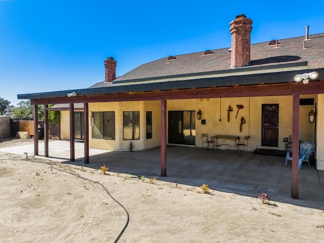 rear view of property with stucco siding, a chimney, fence, and a patio