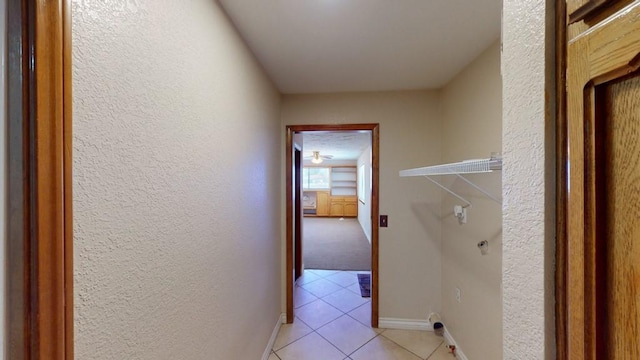 corridor featuring light tile patterned flooring, a textured wall, and baseboards