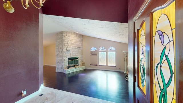 unfurnished living room with baseboards, wood finished floors, vaulted ceiling, a textured ceiling, and a stone fireplace