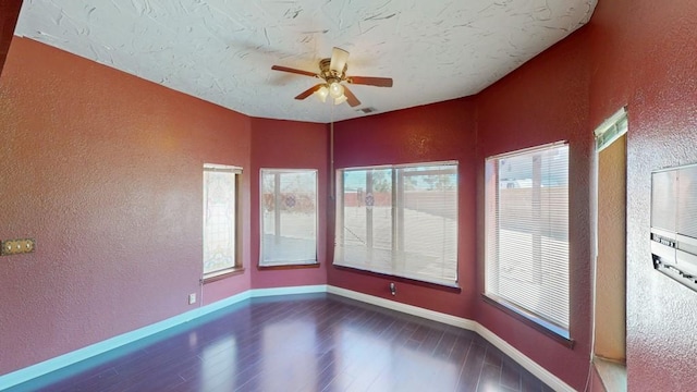 empty room with a textured wall, plenty of natural light, wood finished floors, and a ceiling fan