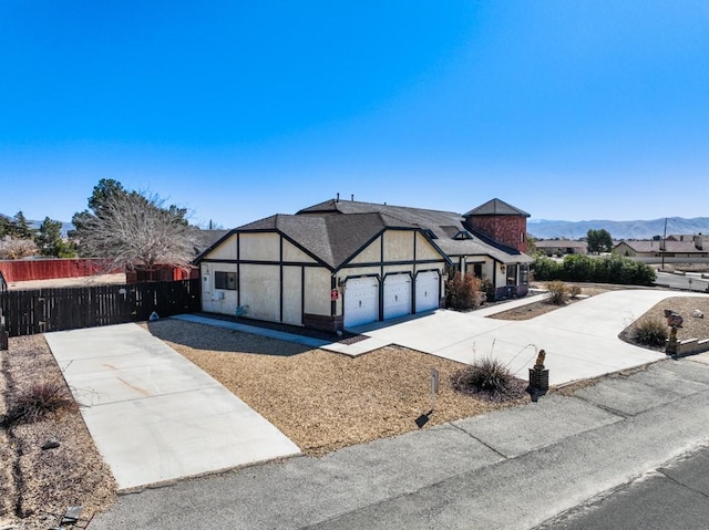 tudor home featuring a garage, driveway, fence, and a mountain view