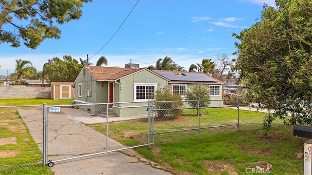 view of front of home with a fenced front yard, a front yard, roof mounted solar panels, an outdoor structure, and a gate