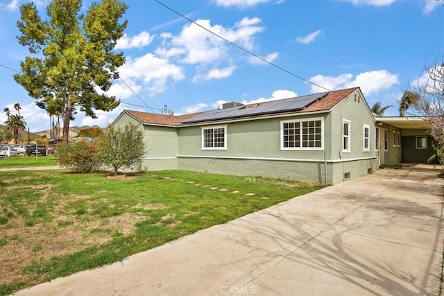 view of side of property with an attached carport, a yard, roof mounted solar panels, and driveway