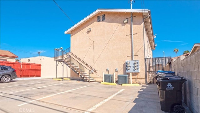 exterior space featuring stairway, fence, central AC unit, and stucco siding