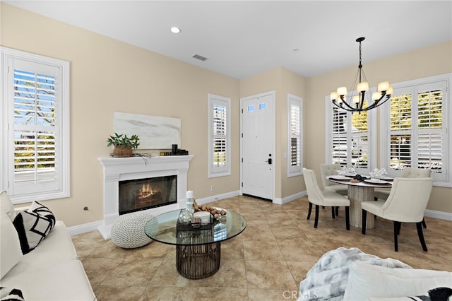 living room with visible vents, a notable chandelier, a healthy amount of sunlight, and a glass covered fireplace