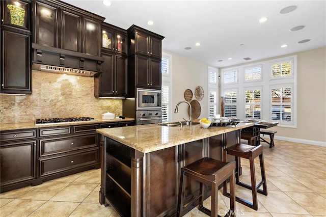 kitchen with a sink, stainless steel appliances, a breakfast bar area, light tile patterned floors, and decorative backsplash