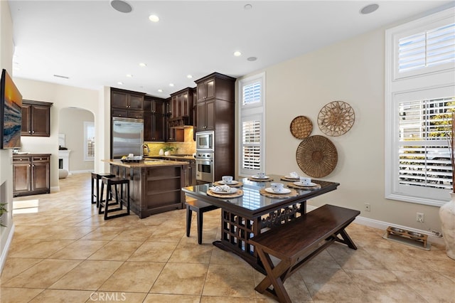 dining space featuring arched walkways, recessed lighting, baseboards, and light tile patterned flooring