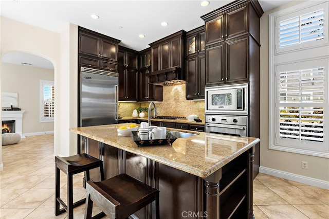 kitchen with plenty of natural light, backsplash, arched walkways, built in appliances, and light stone countertops