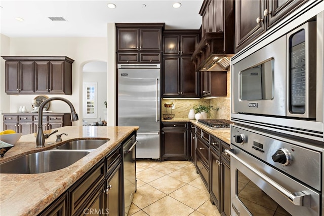 kitchen featuring light stone counters, visible vents, a sink, built in appliances, and tasteful backsplash