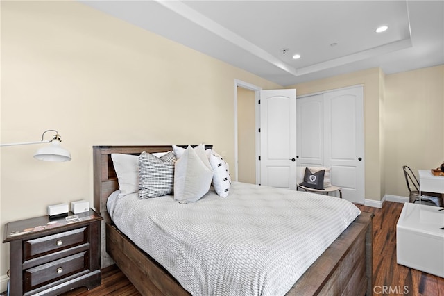 bedroom with recessed lighting, a closet, a raised ceiling, and wood finished floors