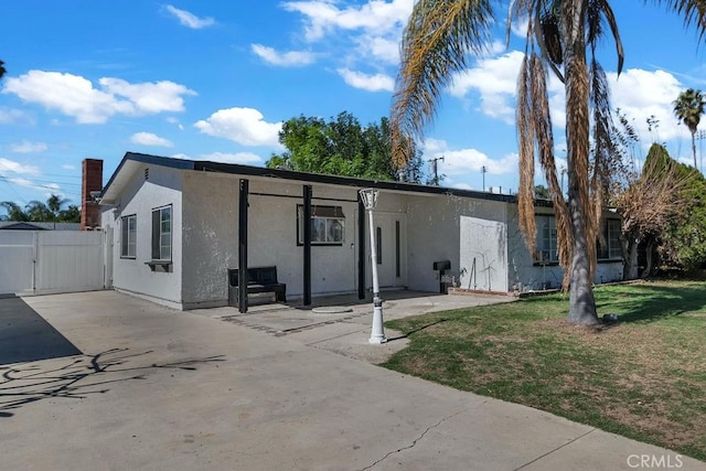 view of front facade featuring stucco siding, a front yard, a gate, a patio area, and fence