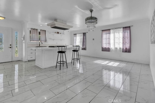 kitchen featuring a breakfast bar area, marble finish floor, light countertops, crown molding, and a sink