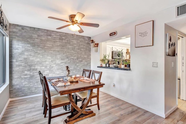 dining room with an accent wall, light wood-type flooring, visible vents, and baseboards