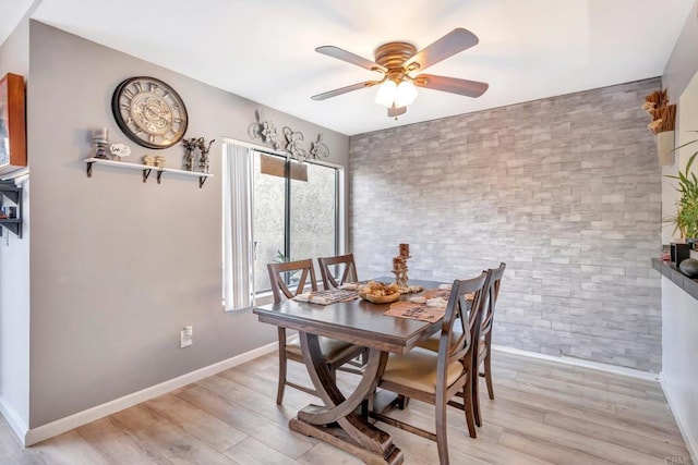 dining area featuring ceiling fan, brick wall, light wood-style flooring, and baseboards