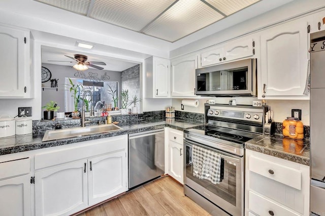 kitchen with ceiling fan, stainless steel appliances, a sink, white cabinetry, and light wood-type flooring