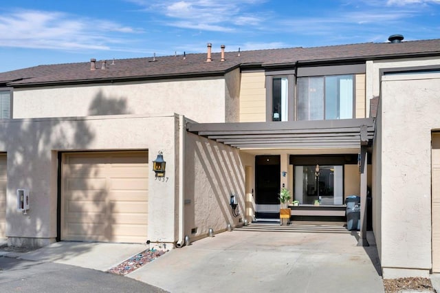 rear view of house with driveway, a shingled roof, and stucco siding