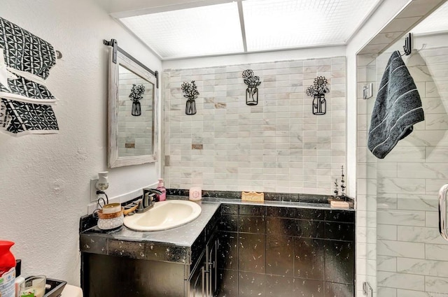 full bathroom with a textured wall, a tile shower, and vanity