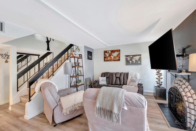 living room with a fireplace, visible vents, baseboards, stairway, and light wood finished floors