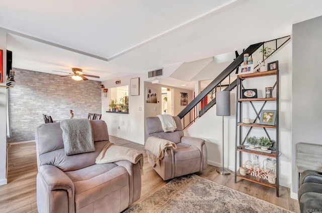 living area featuring brick wall, light wood-style flooring, stairs, and visible vents