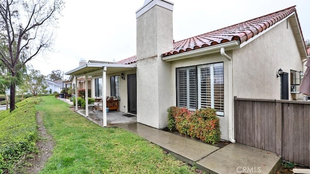 exterior space with stucco siding, a tile roof, a patio, a yard, and a chimney