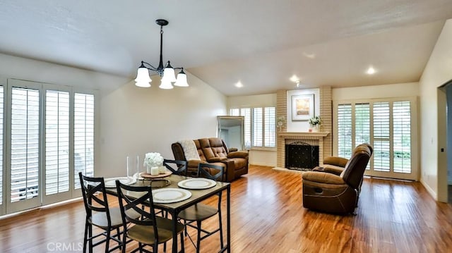 dining room with a healthy amount of sunlight, a brick fireplace, wood finished floors, and vaulted ceiling