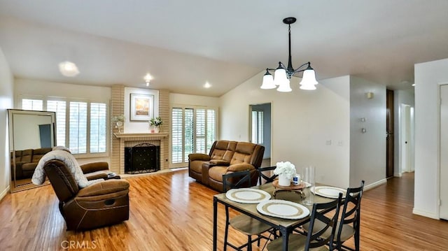 dining area featuring a brick fireplace, baseboards, a chandelier, vaulted ceiling, and light wood-style floors