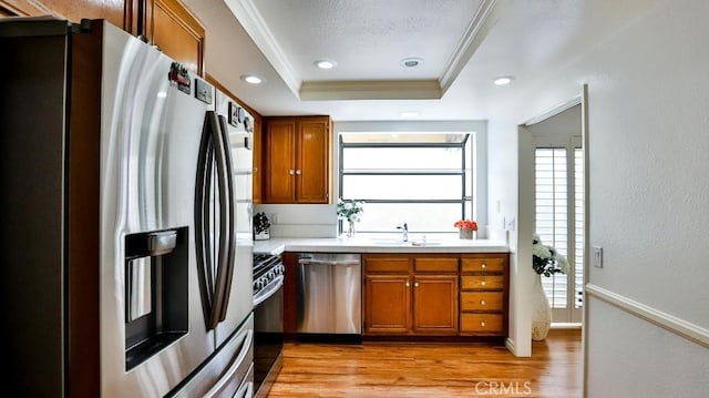 kitchen featuring appliances with stainless steel finishes, light wood-style floors, brown cabinetry, a raised ceiling, and a sink