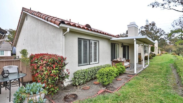 view of property exterior featuring stucco siding, a lawn, a tile roof, a patio, and a chimney