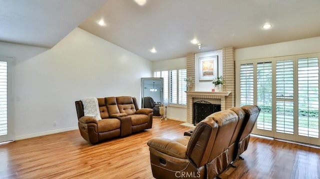 living area with vaulted ceiling, a brick fireplace, wood finished floors, and baseboards