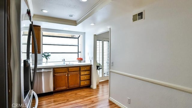 bar featuring visible vents, light wood-type flooring, a sink, a tray ceiling, and appliances with stainless steel finishes