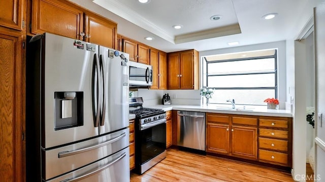 kitchen featuring brown cabinetry, a tray ceiling, a sink, stainless steel appliances, and light countertops