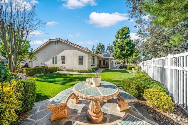 back of property featuring a patio, stucco siding, a lawn, roof mounted solar panels, and fence private yard