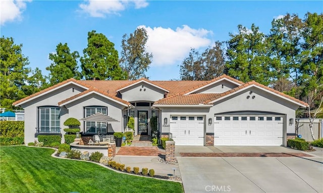 mediterranean / spanish home featuring a garage, fence, concrete driveway, stucco siding, and a front lawn