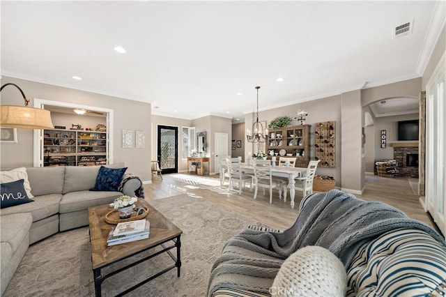 living room with a fireplace, crown molding, recessed lighting, visible vents, and light wood-style floors