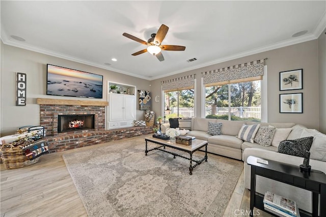 living room featuring a brick fireplace, visible vents, crown molding, and wood finished floors