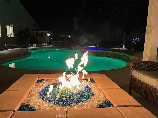 pool at night with an outdoor pool and a fire pit