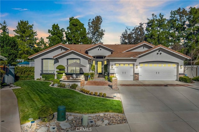 mediterranean / spanish-style house with a tile roof, a yard, stucco siding, concrete driveway, and fence