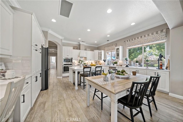 dining room featuring arched walkways, baseboards, ornamental molding, light wood-type flooring, and recessed lighting