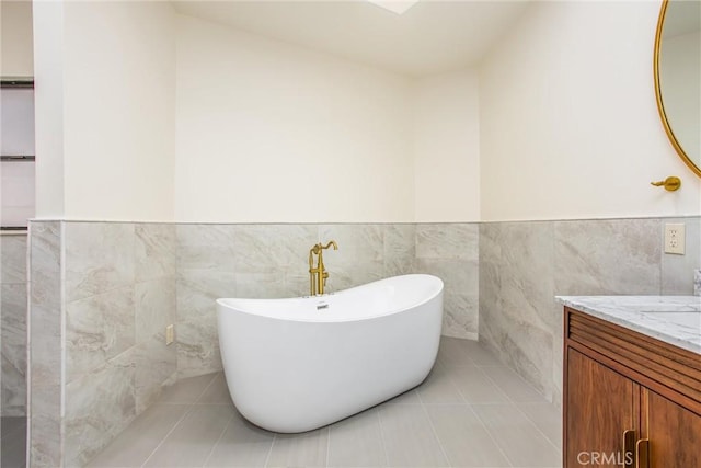 full bathroom with a wainscoted wall, tile walls, a soaking tub, vanity, and tile patterned floors