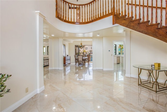 entrance foyer featuring baseboards, stairway, marble finish floor, a high ceiling, and a notable chandelier