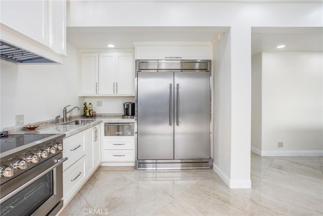 kitchen featuring baseboards, white cabinets, premium appliances, light stone countertops, and a sink