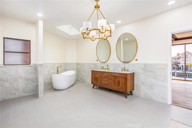 bathroom featuring double vanity, tile patterned floors, an inviting chandelier, a freestanding tub, and tile walls