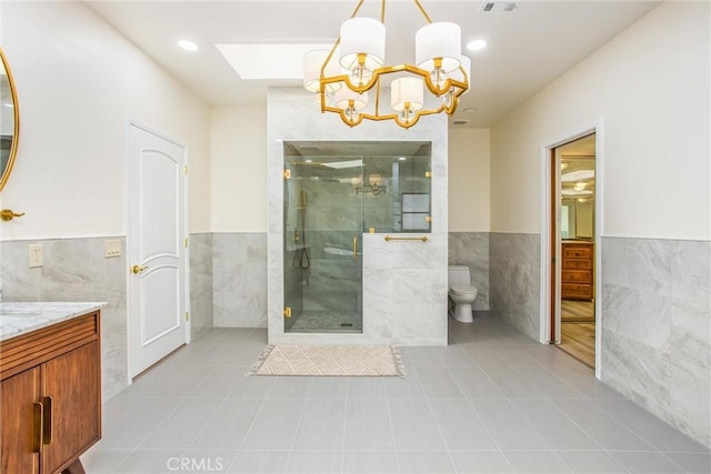 full bath featuring a stall shower, vanity, tile walls, and wainscoting